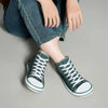 Mujer sentada usando zapatillas barefoot mujer verdes de lona con jeans.